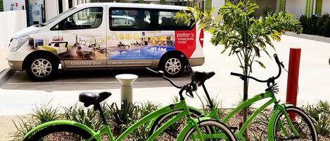 A courtyard with a white van advertising a motel, two green bicycles, and a small tree.