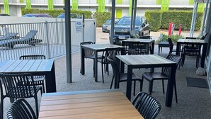 An outdoor seating area with tables and chairs, a covered walkway, and a pool in the background. - Mackay Oceanside Central Hotel (East Mackay)