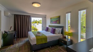 A hotel room with a bed, desk, and a view of greenery outside. - Mackay Oceanside Central Hotel (East Mackay)