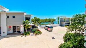 A parking area with a white van, a building entrance with a sign, and a small kiosk. - Mackay Oceanside Central Hotel (East Mackay)