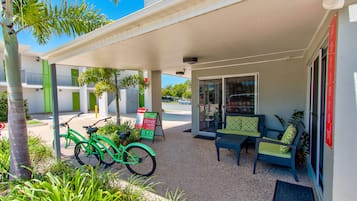 A covered outdoor seating area with a table and chairs, a green bicycle, and a signboard.