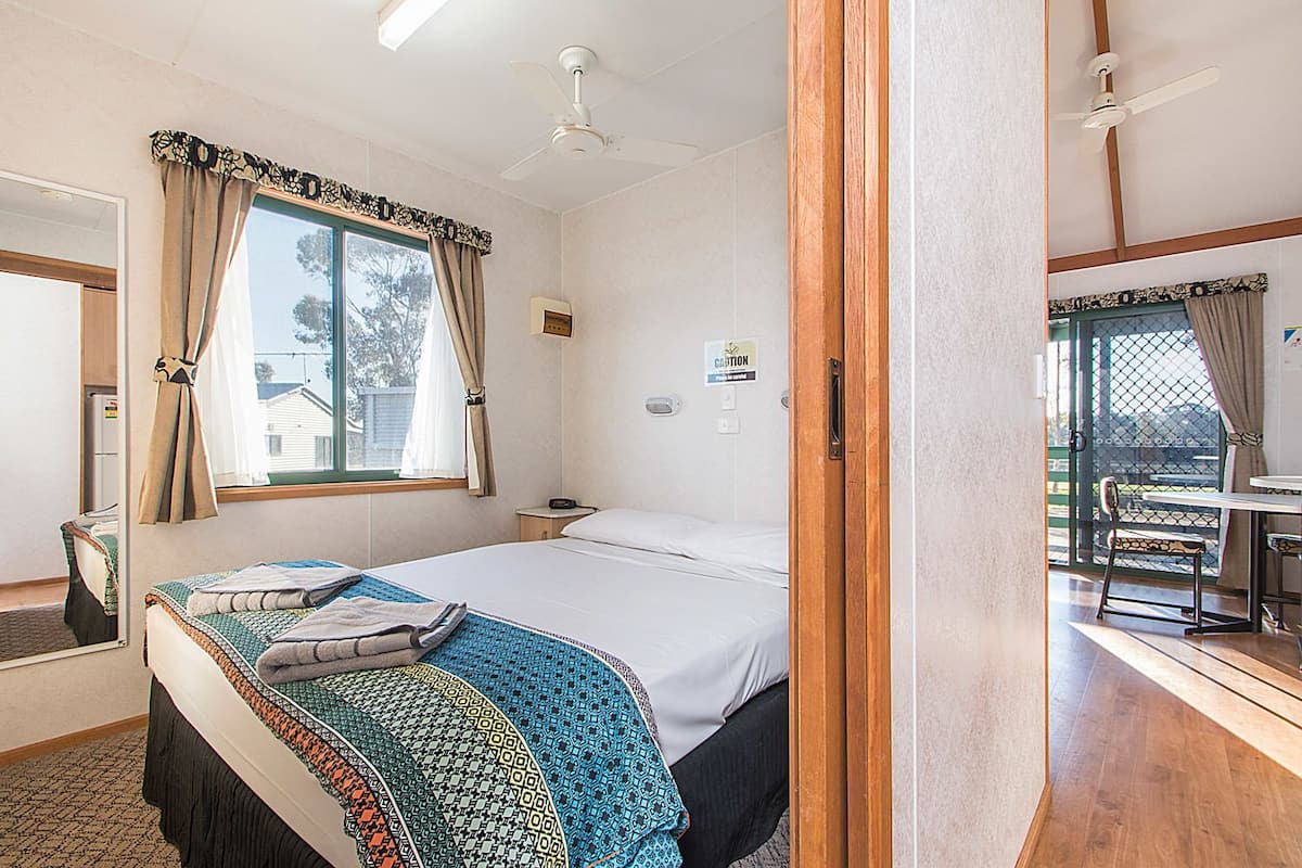 A bedroom with a bed, a window with curtains, a bedside table, and a view of an outdoor area with a table and chairs.