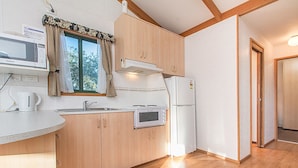 Eine kompakte Küche mit Holzausstattung, einer Mikrowelle, einem Kühlschrank und einem Fenster mit Vorhängen.