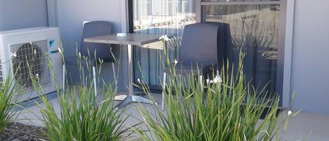 An outdoor seating area with a table and chairs, a glass door, and a small garden with plants.