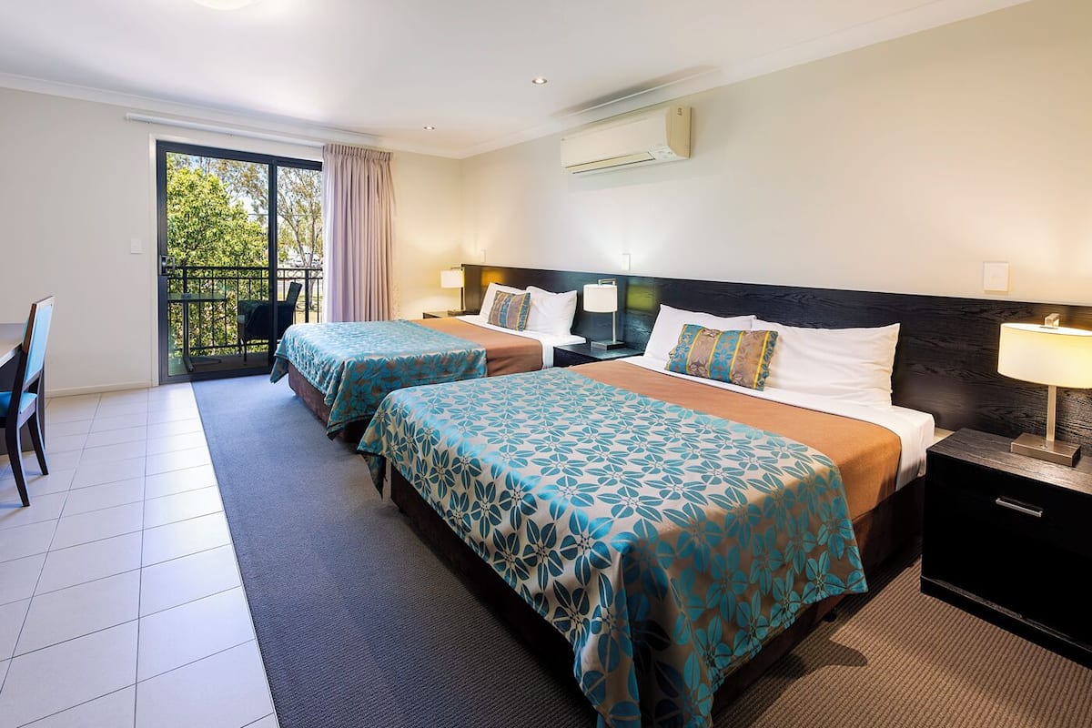Habitación de hotel con dos camas, un balcón, zona de comedor y aire acondicionado.