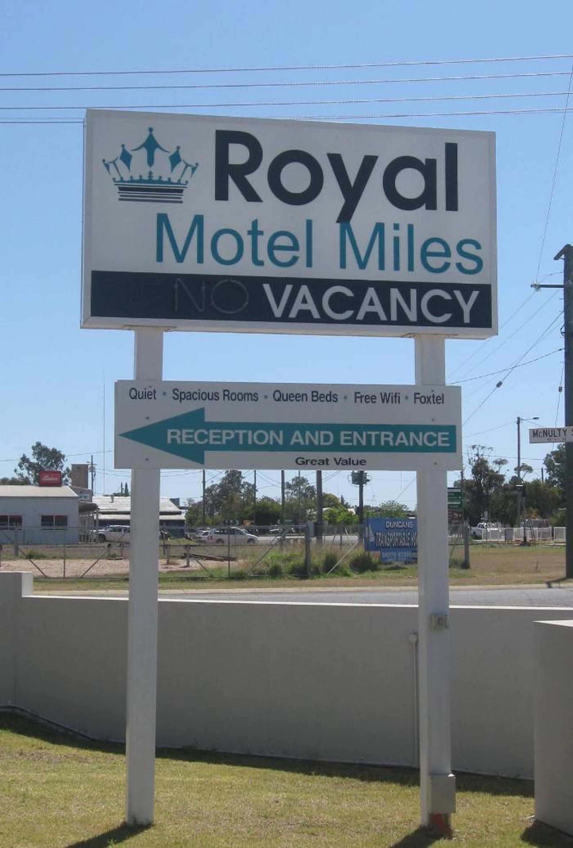 Señal del Royal Motel Miles con un logotipo de corona, que indica 'NO DISPONIBLE' y destaca comodidades como habitaciones tranquilas, espaciosas, camas queen, wifi gratuito y Foxtel.