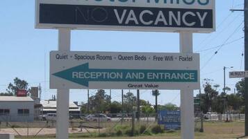 Señal del Royal Motel Miles con un logotipo de corona, que indica 'NO DISPONIBLE' y destaca comodidades como habitaciones tranquilas, espaciosas, camas queen, wifi gratuito y Foxtel.