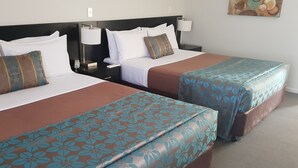 Twee eenpersoonsbedden met bruin en blauw bloemenbeddengoed, witte kussens en een nachtkastje met lamp en telefoon.