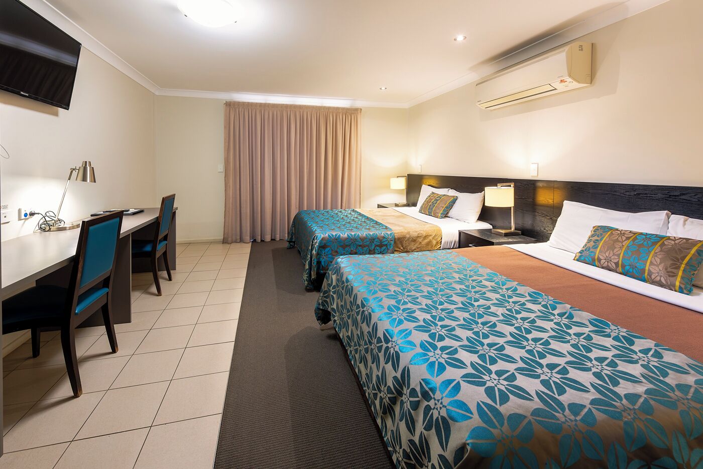 Une chambre d’hôtel équipée d’un bureau, de deux lits, d’une télévision et d’un appareil de climatisation.