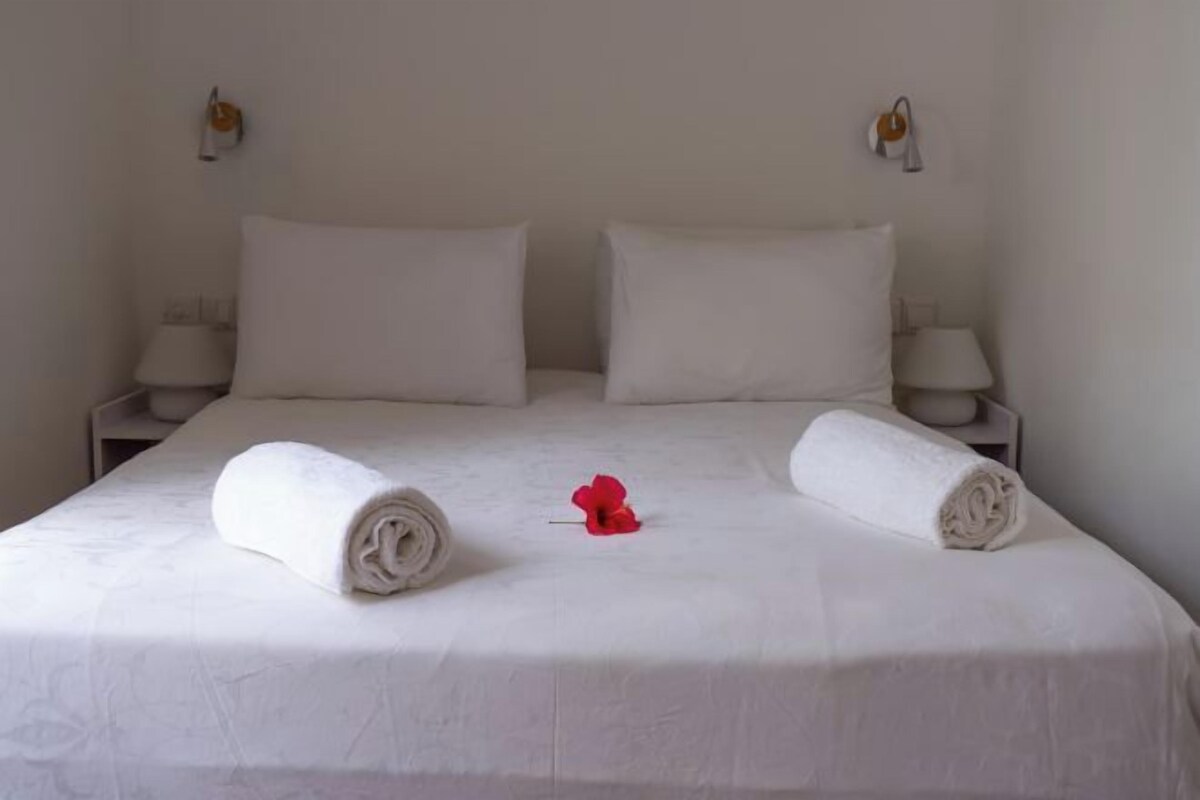 A neatly made bed with two rolled white towels and a red flower.