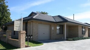 A single-story building with a flat roof, a garage door, and a small porch area. - Breakaway Apartments (Cowra)