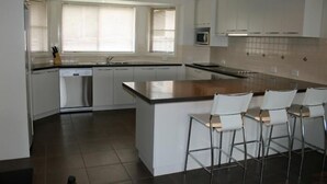 A modern kitchen with white cabinets, a central island with bar stools, a dishwasher, and a microwave. - Breakaway Apartments (Cowra)