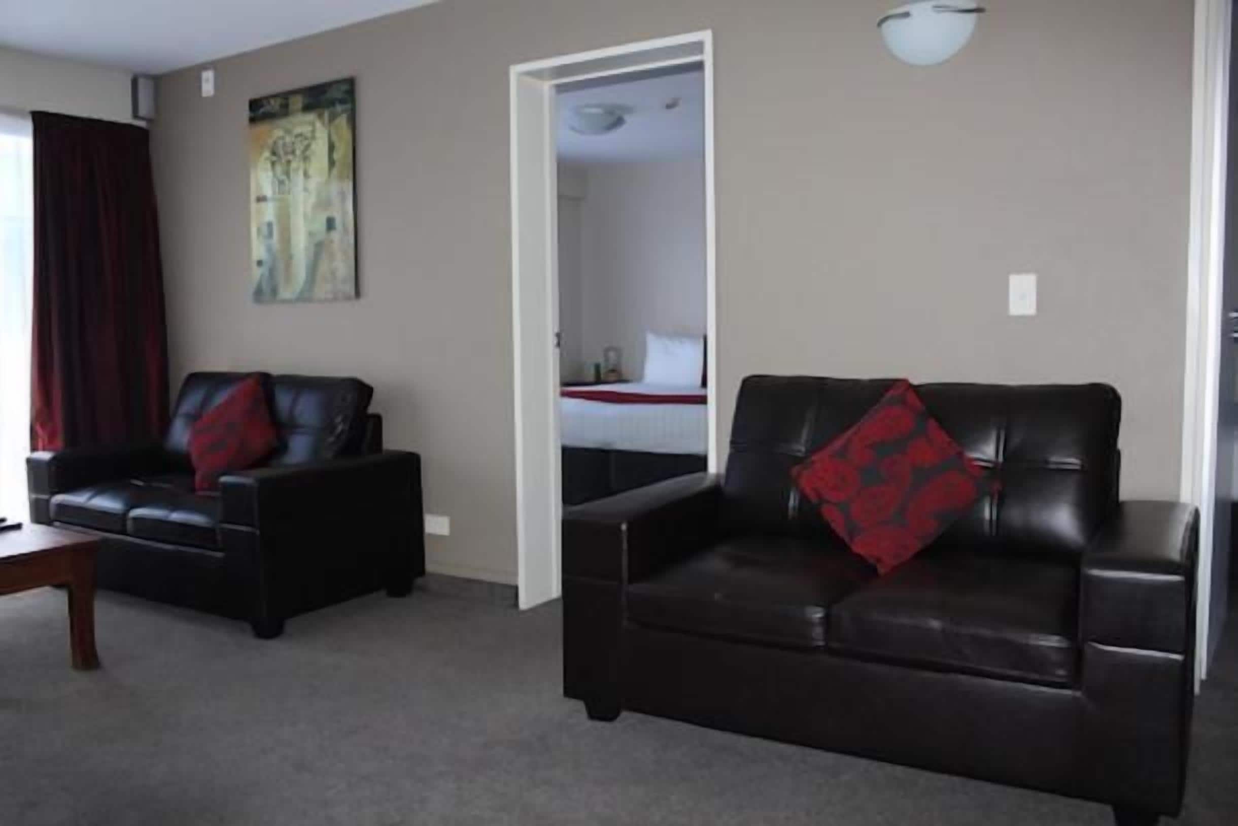 A living room with two black leather sofas, one with a red pillow, and a painting on the wall.