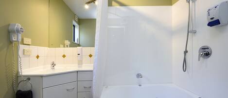 Un bagno con una vasca da bagno bianca, una doccia, un lavandino e un asciugacapelli.