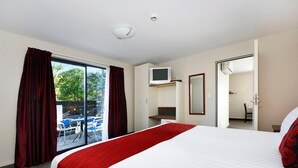 A hotel room with a large bed, a TV, a sliding door to a balcony, and a view of the outdoors. - Gladstone Motel Nelson (Richmond)