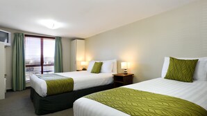 A hotel room with two beds, green and white bedding, bedside lamps, a window with curtains, and a wall-mounted TV. - Gladstone Motel Nelson (Richmond)