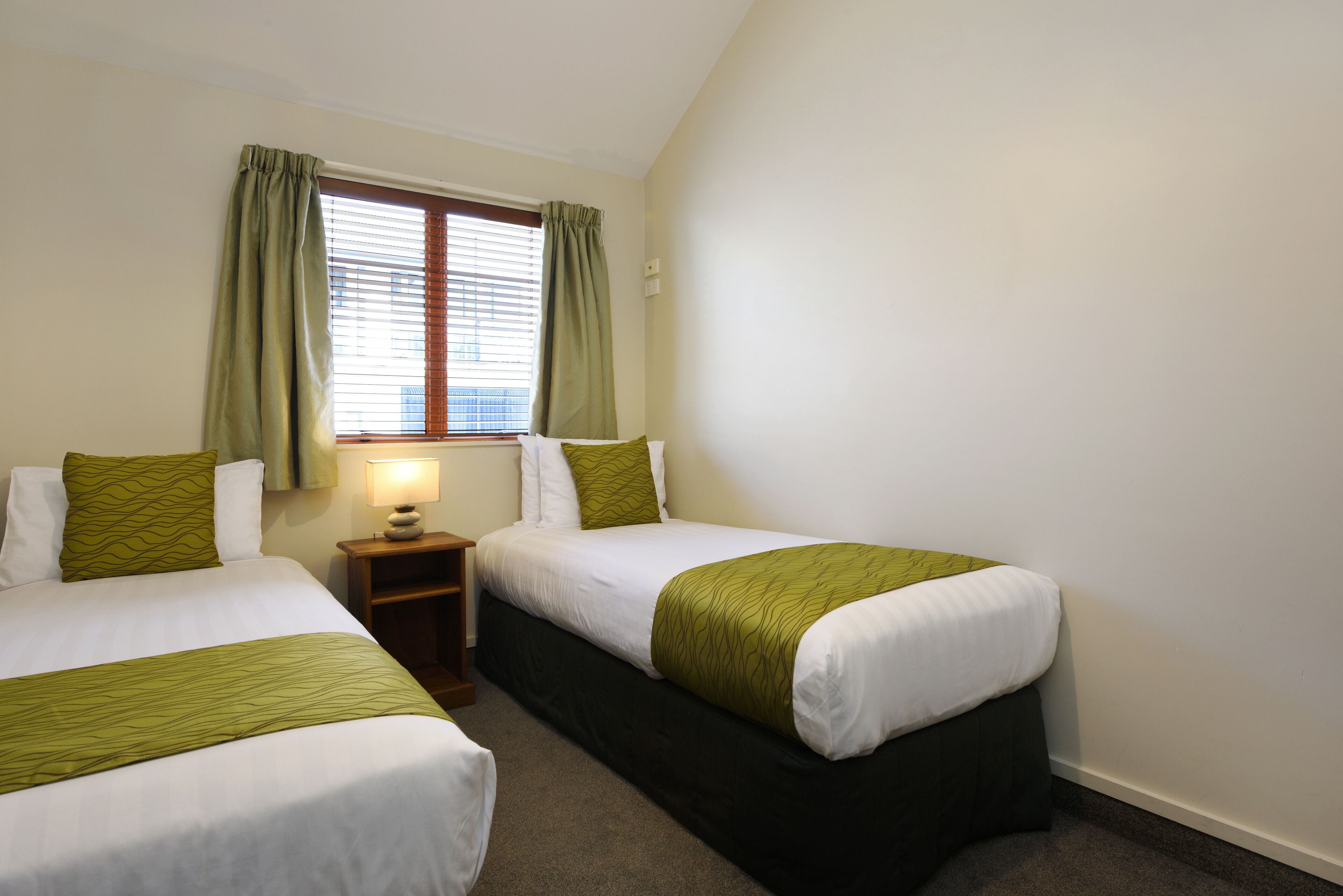 Een hotelkamer met twee bedden, een nachtkastje, een lamp en een raam met gordijnen.