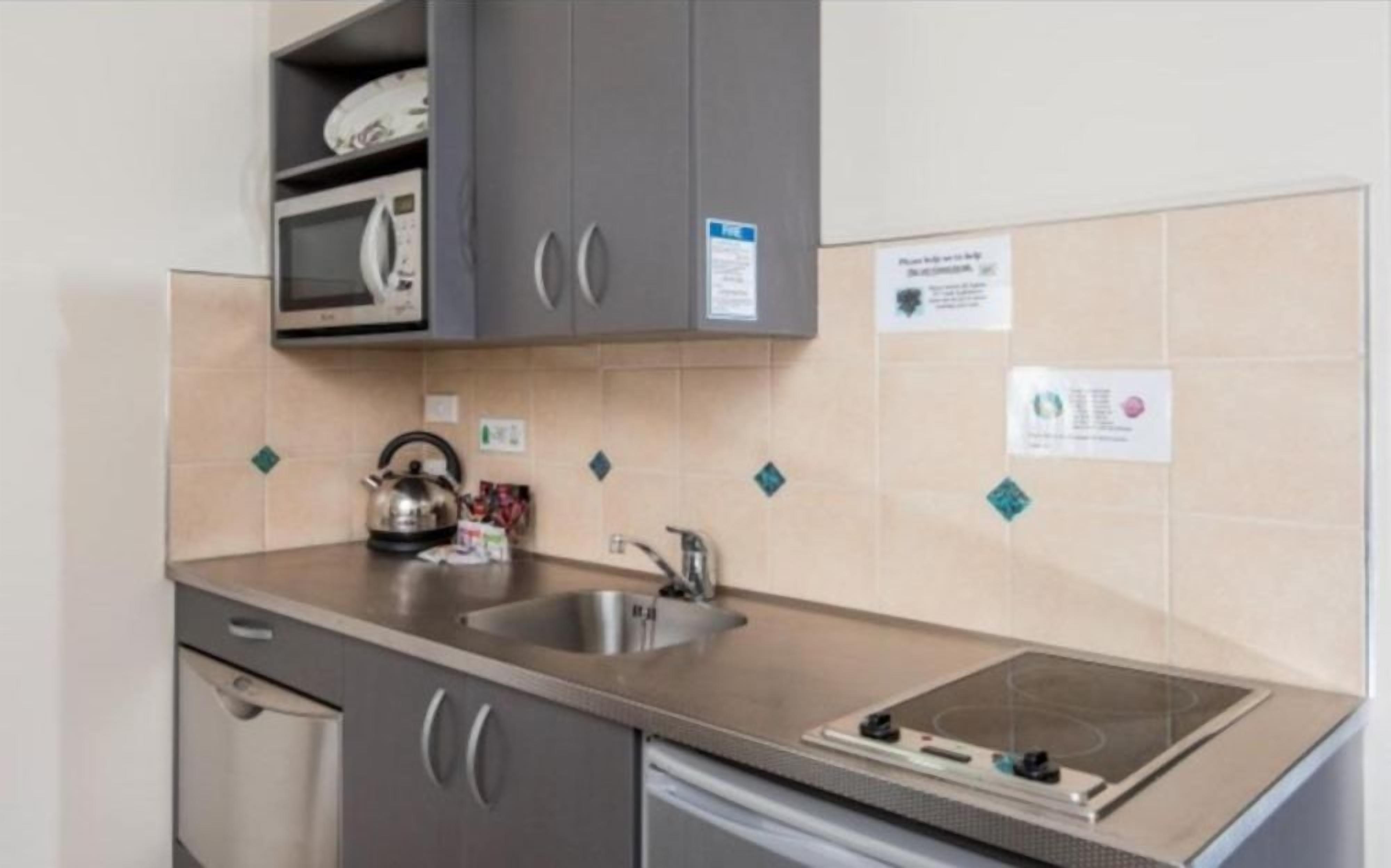 A kitchen with a microwave, kettle, sink, and a built-in stovetop.