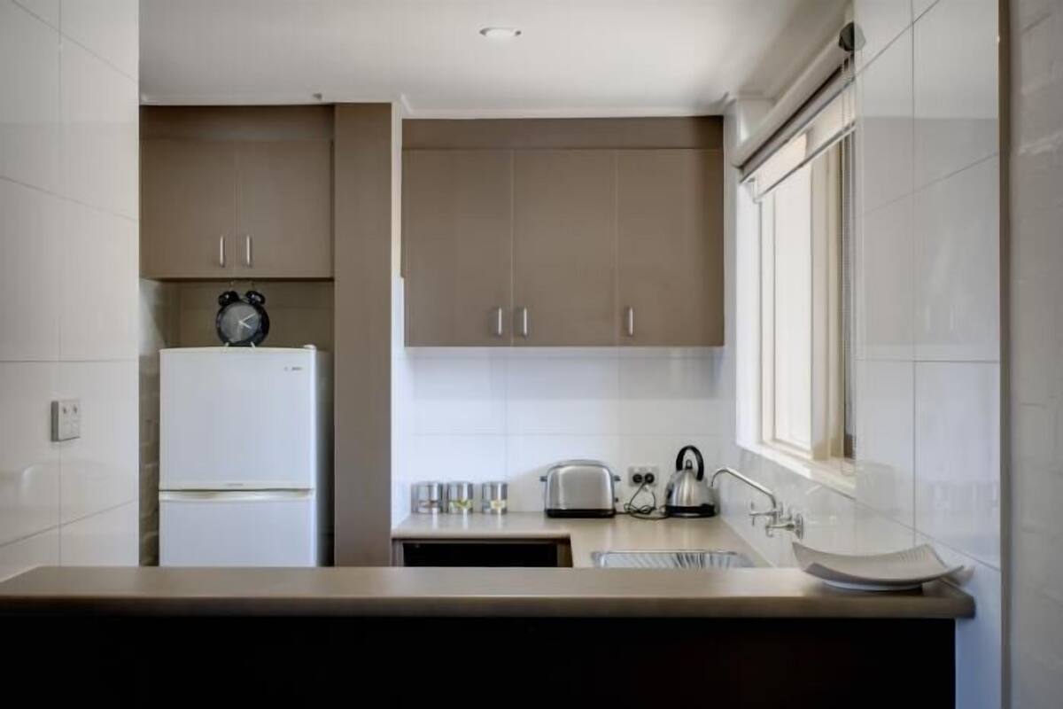 Una cocina moderna con armarios blancos, horno empotrado, hervidor y tostadora.