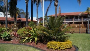 A hotel with a red-tiled roof, palm trees, and a well-maintained garden with various plants and a fountain.