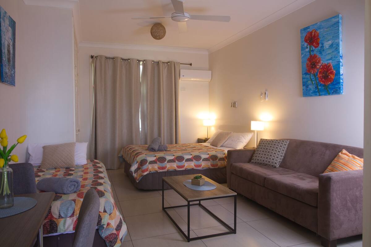 A hotel room with a bed, two bedside tables with lamps, a sofa, a coffee table, and a ceiling fan.