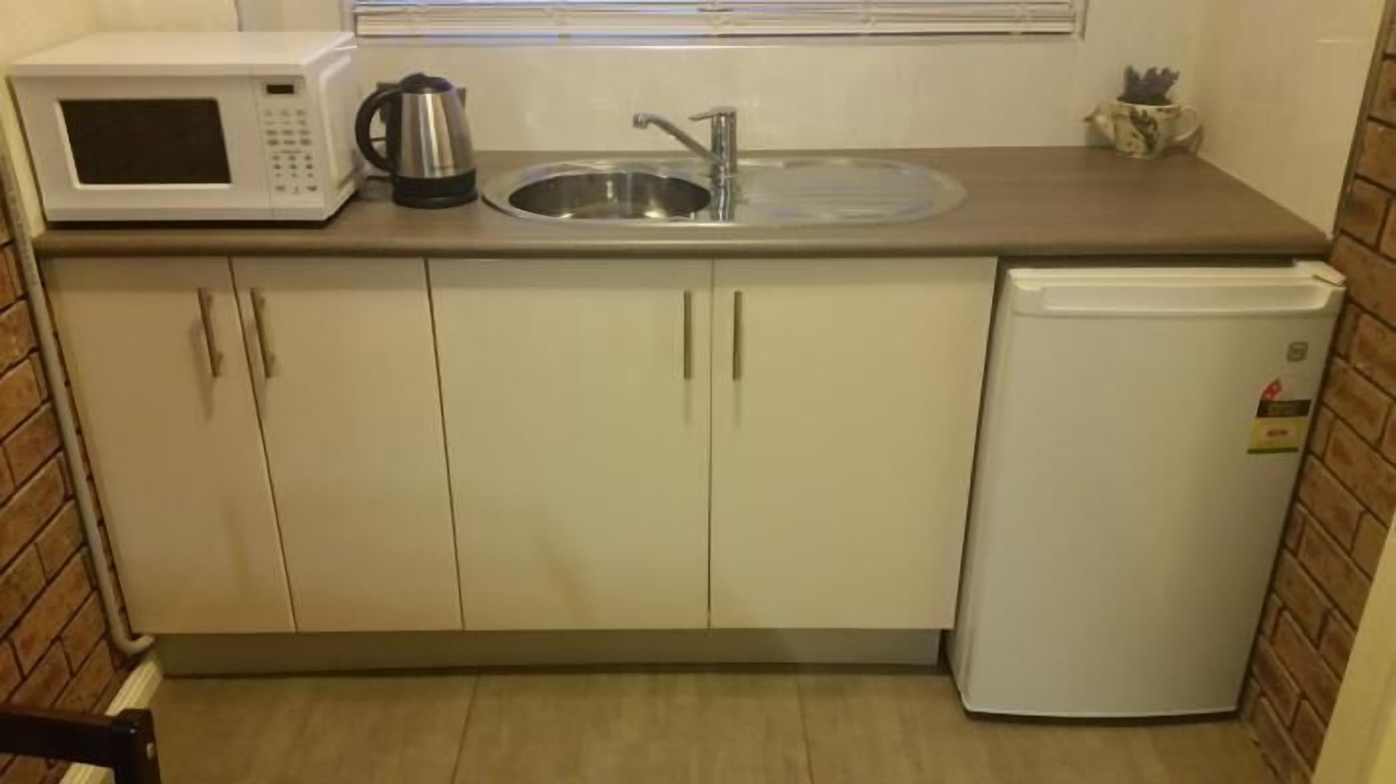 A compact kitchenette with a microwave, kettle, sink, and a small refrigerator.