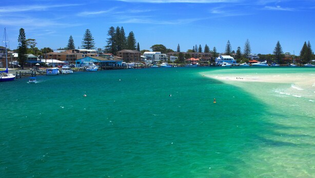A coastal area with clear turquoise waters, a sandy beach, and several boats docked near a marina.