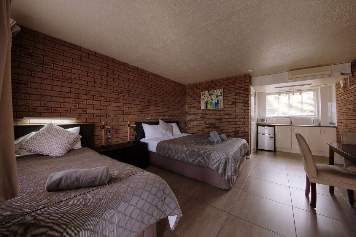 A room with two beds, a small kitchenette, and a dining area.