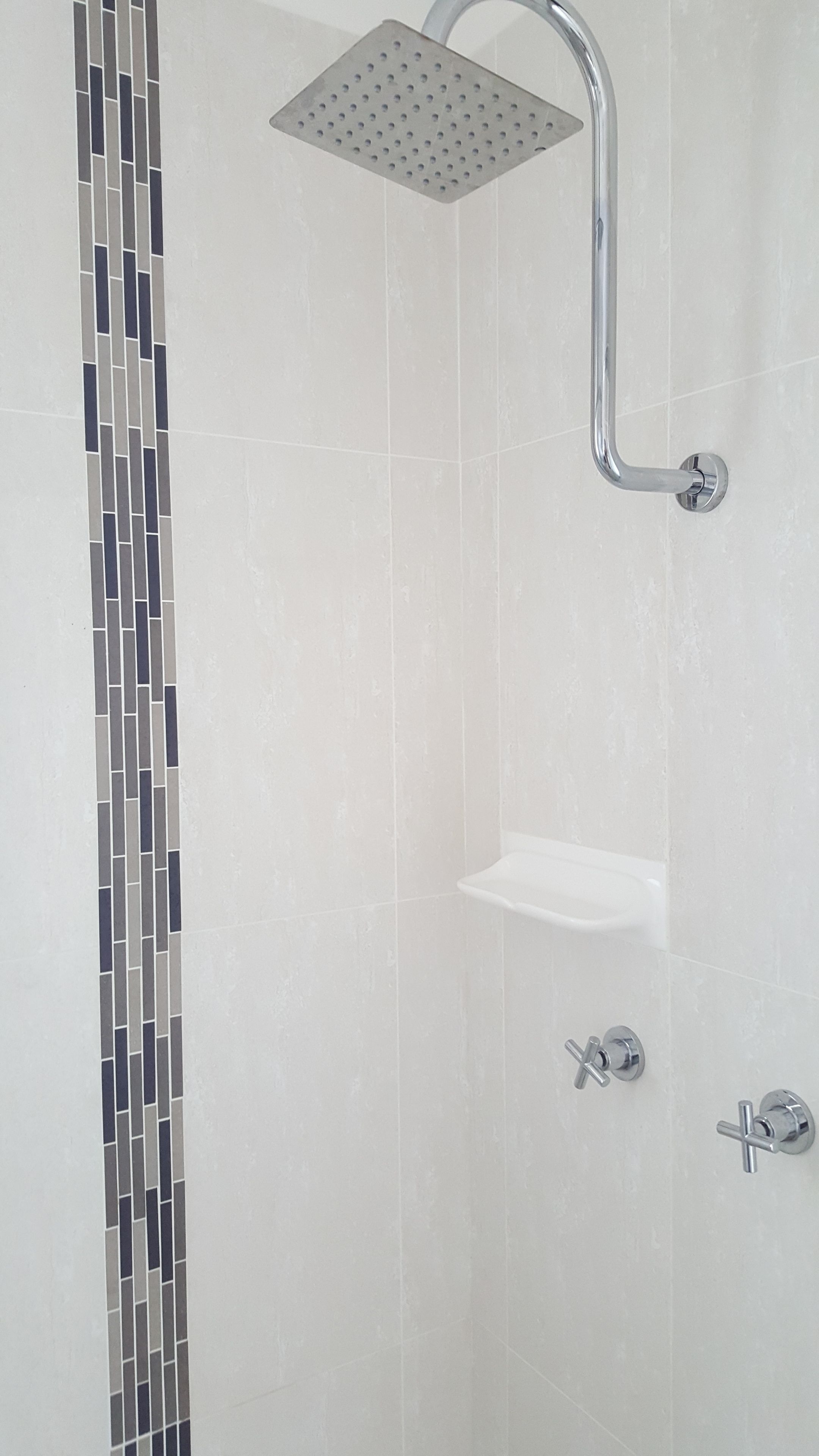 A shower with a square head, a chrome handle, and a wall-mounted shelf.