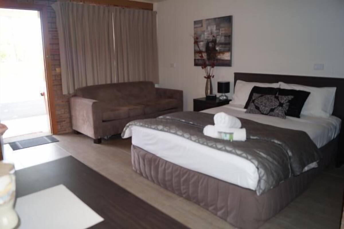 A hotel room with a bed, a sofa, a nightstand, and a painting on the wall.