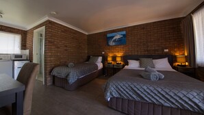 A hotel room with two beds, a kitchenette, and a brick wall.