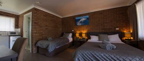 A hotel room with two beds, a kitchenette, and a brick wall.