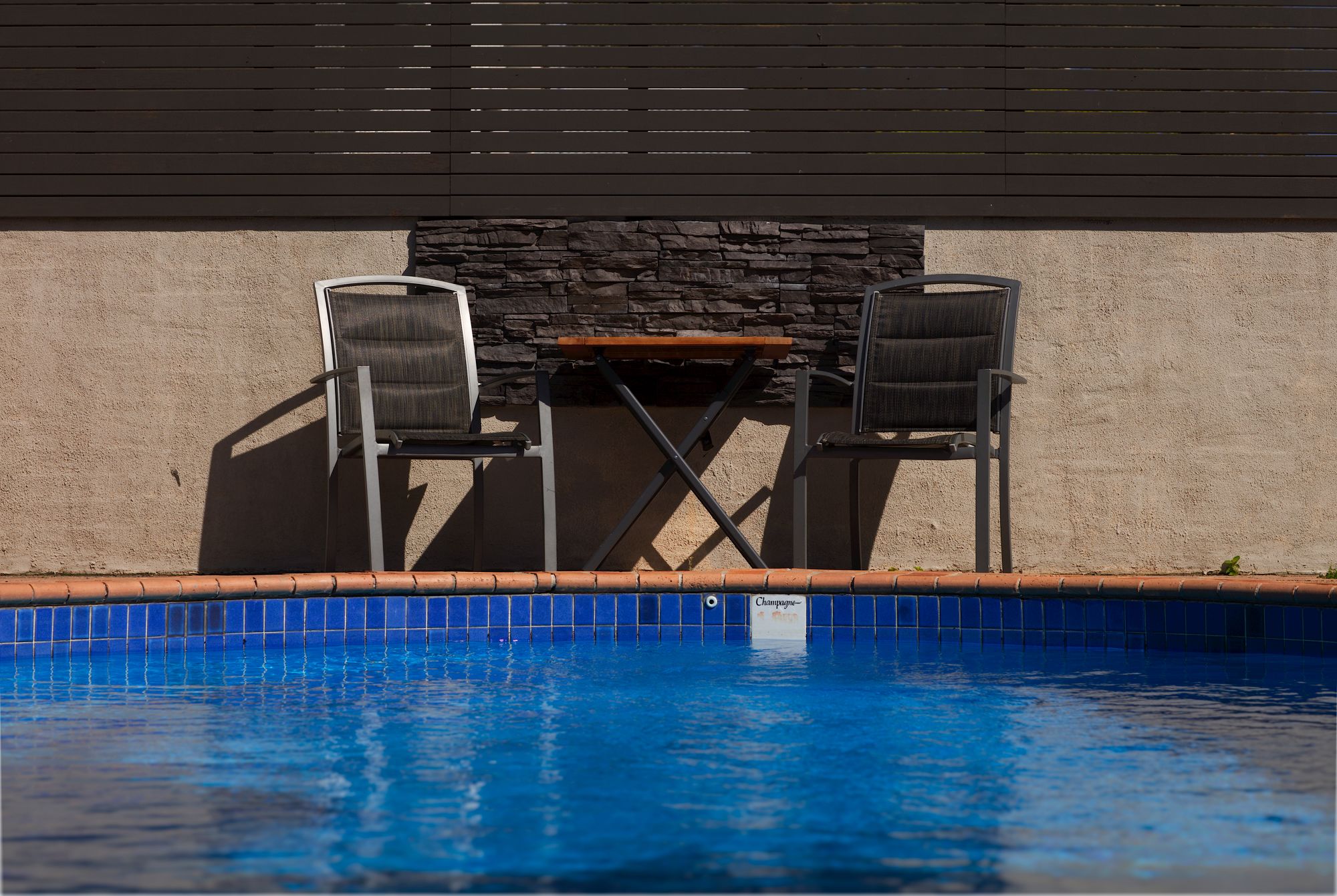 A pool area with two chairs and a table against a stone wall.
