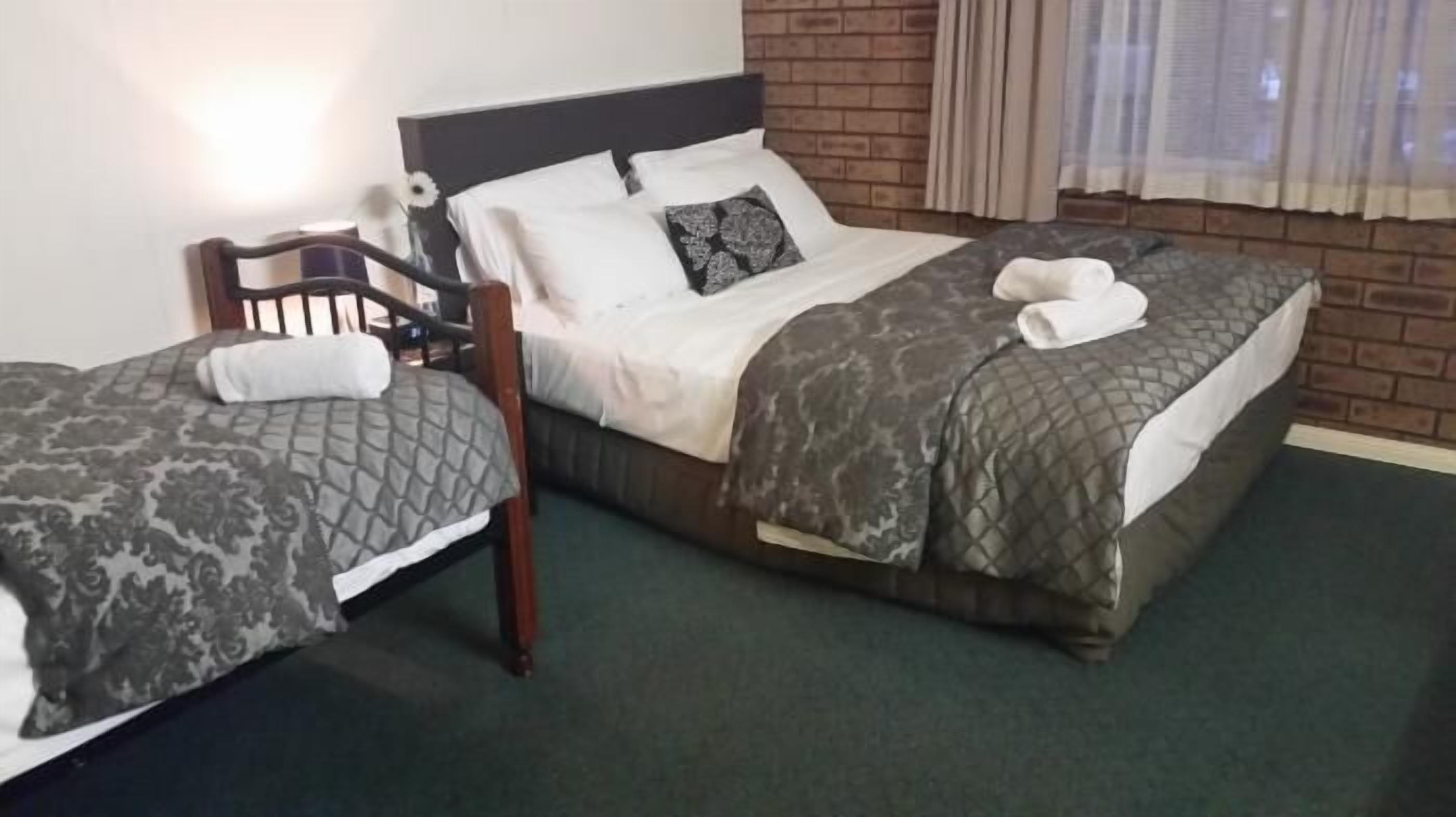 A hotel room with two beds, a wooden chair, and a brick wall.