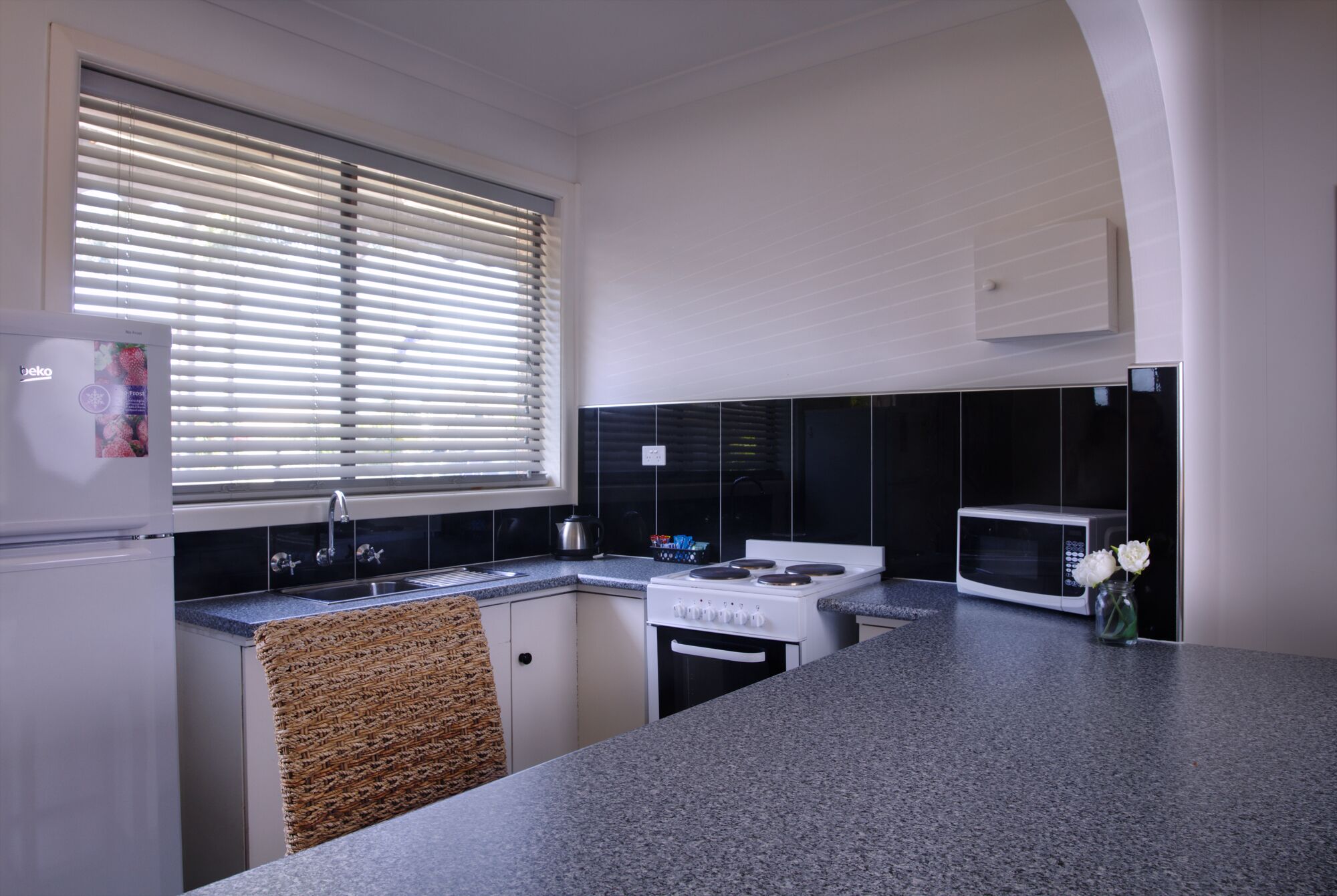 A kitchen with a refrigerator, stove, microwave, and a window with blinds.