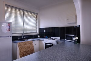 A kitchen with a refrigerator, stove, microwave, and a window with blinds.