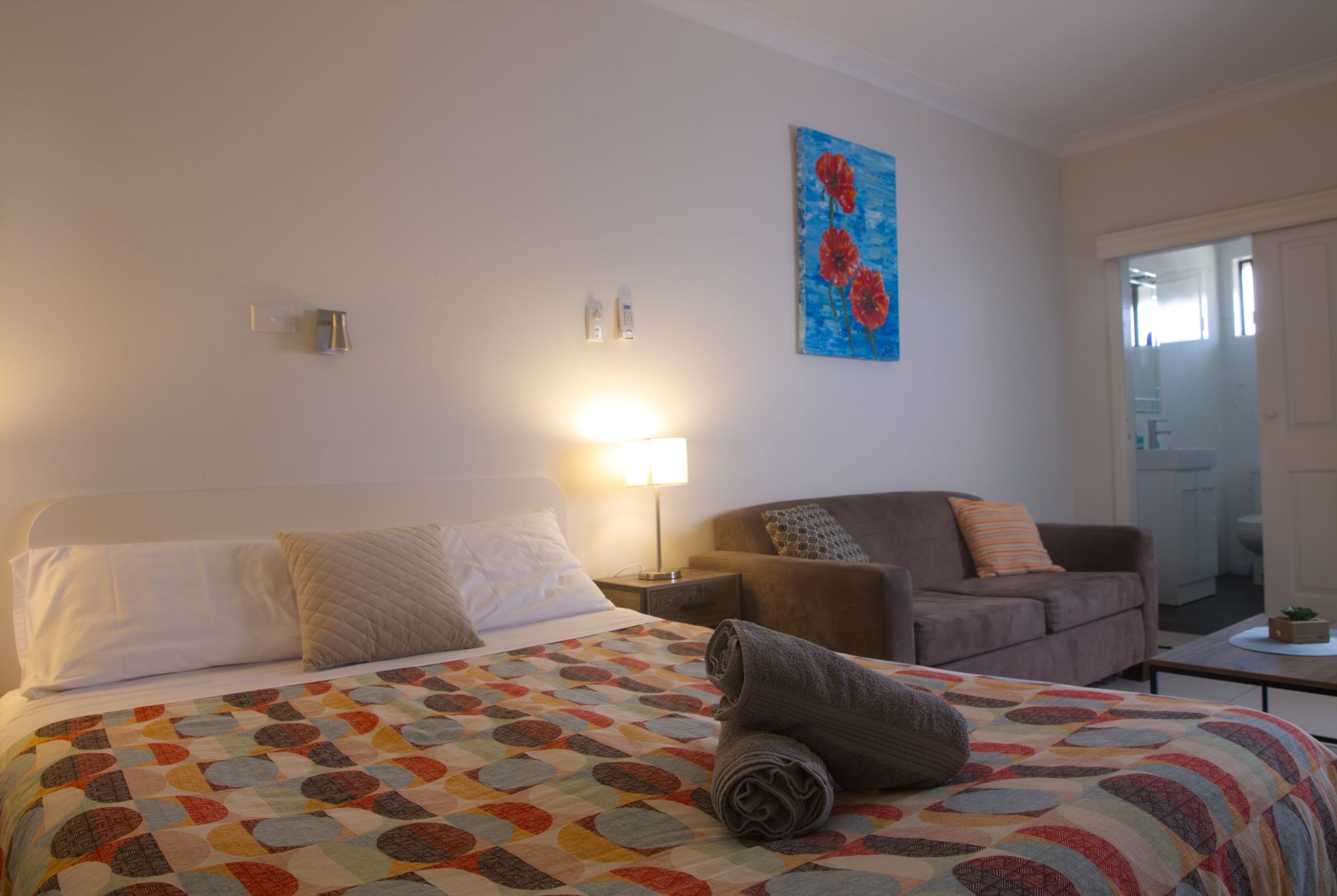 Une chambre d’hôtel avec un lit, une chaise, une table de chevet, une lampe et un tableau au mur.