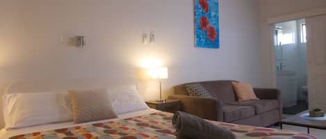 Une chambre d’hôtel avec un lit, une chaise, une table de chevet, une lampe et un tableau au mur.
