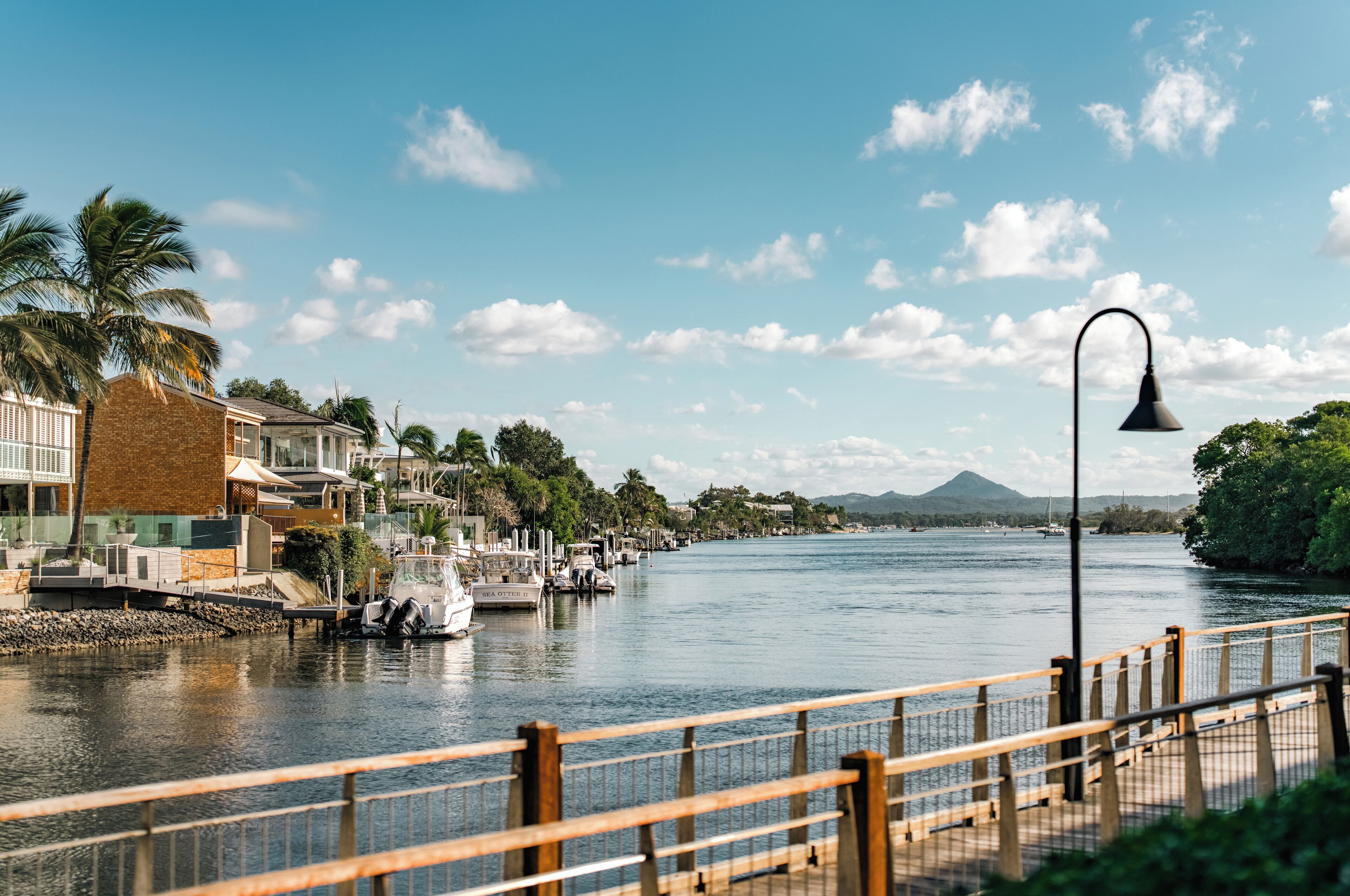 A waterfront view with a wooden walkway, boats docked, and buildings along the riverbank.