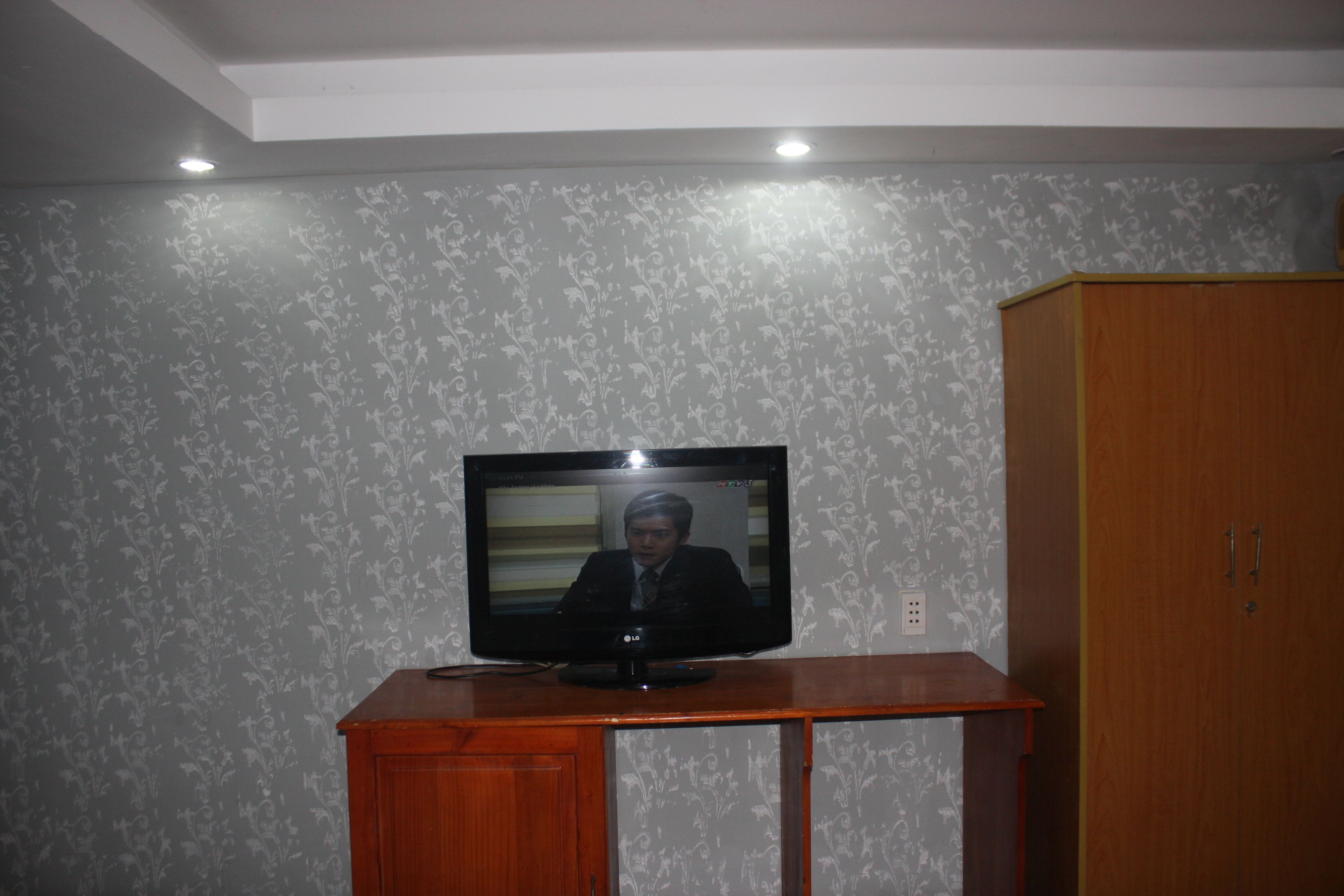 A television on a wooden stand in a room with patterned wallpaper.