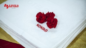 A white towel with red text and three red roses on it, placed on a golden surface. - Koniko hotel (Ho Chi Minh City)