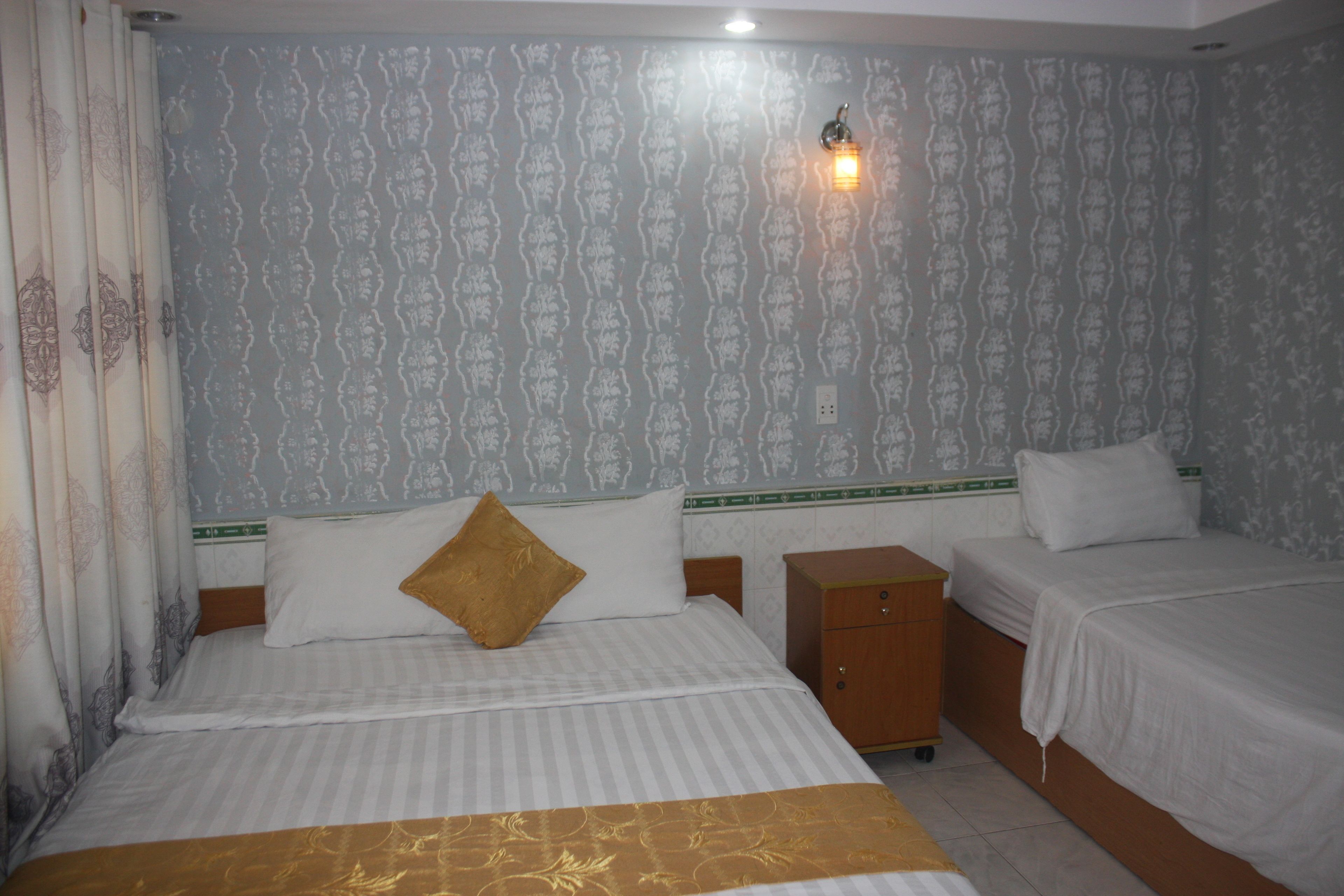 A hotel room with two beds, a nightstand, and a wall-mounted light fixture.