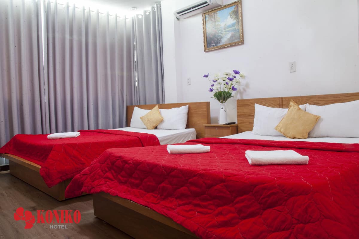 Quarto de hotel com duas camas, cada uma com colcha vermelha e travesseiros brancos. Há um vaso com flores na mesa de cabeceira entre as camas.