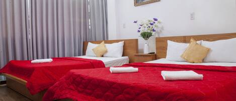 Ein Hotelzimmer mit zwei Betten, jeweils mit roter Bettdecke und weißen Kissen. Auf dem Nachttisch zwischen den Betten steht eine Vase mit Blumen.