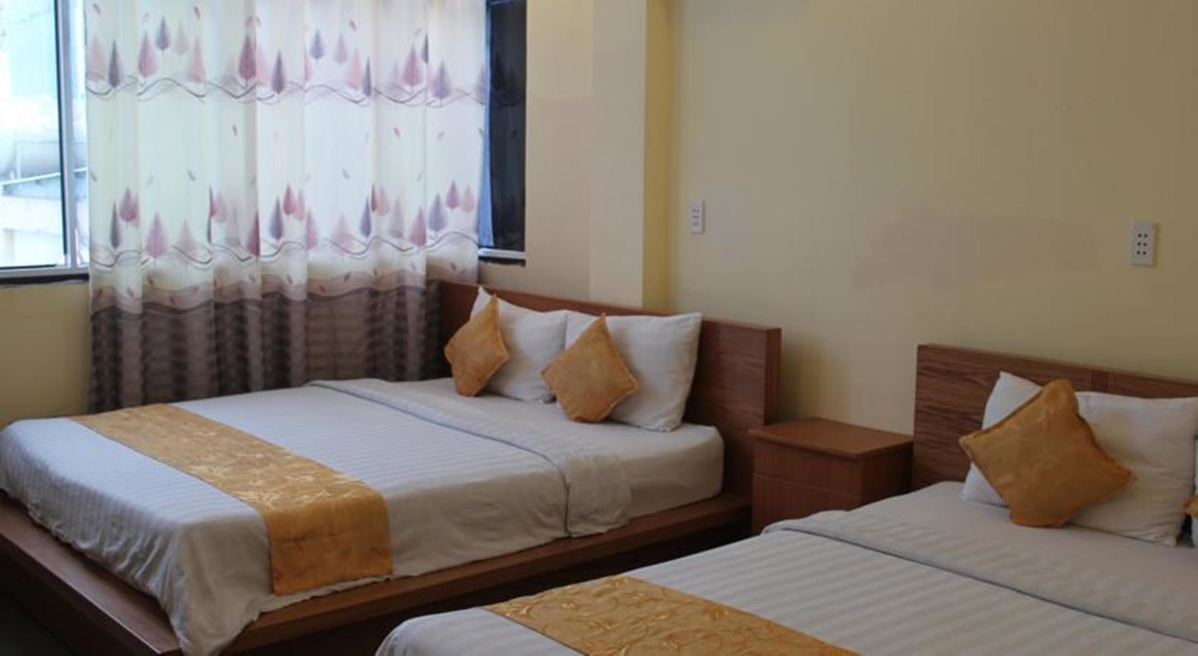 A hotel room with two beds, a window with curtains, and a bedside table.