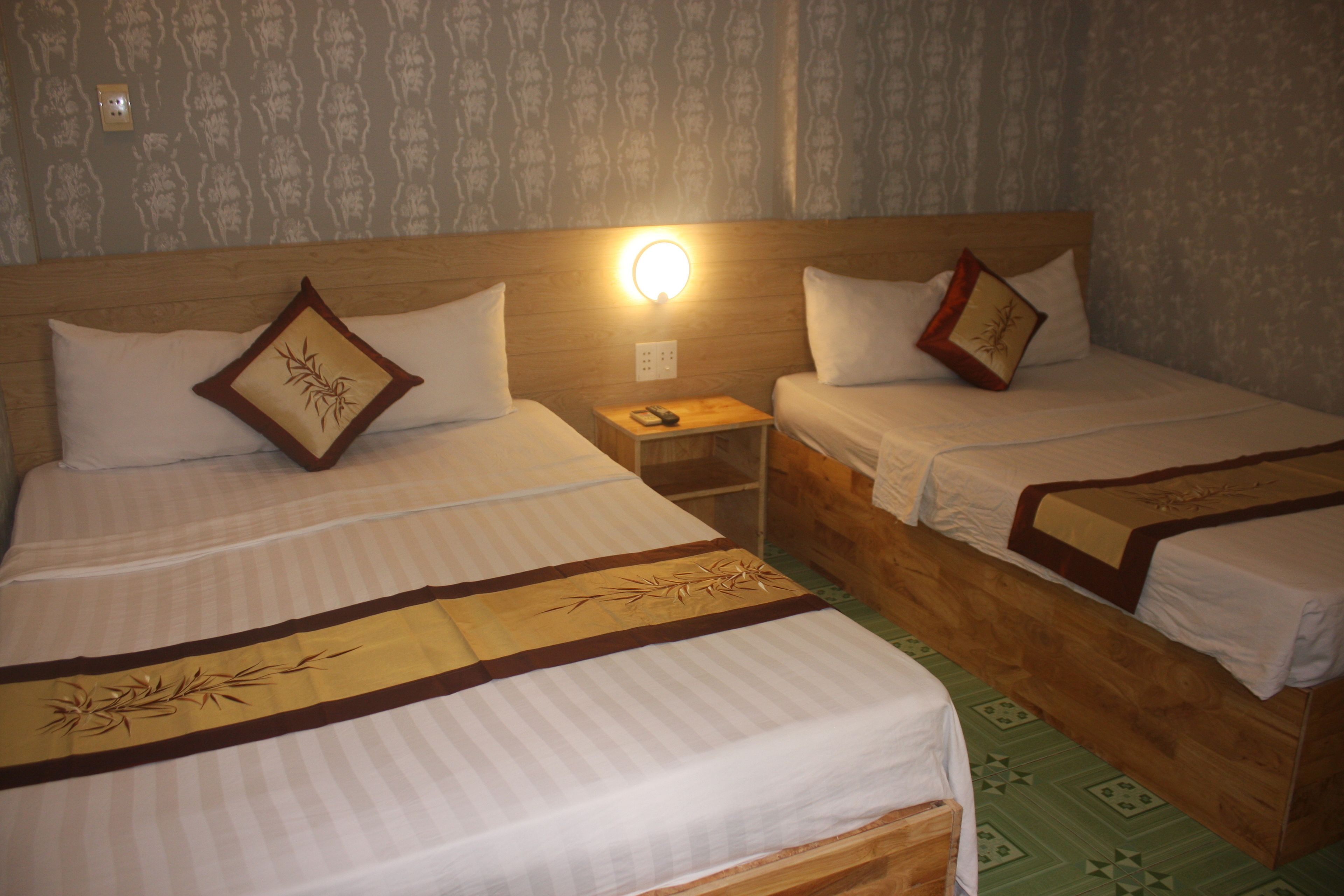 A hotel room with two single beds, each with a wooden headboard, a bedside table, and a wall-mounted light.