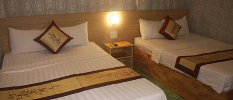 A hotel room with two single beds, each with a wooden headboard, a bedside table, and a wall-mounted light.