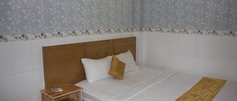 A neatly made bed with a wooden headboard, a bedside table with a remote control, and a patterned wall.