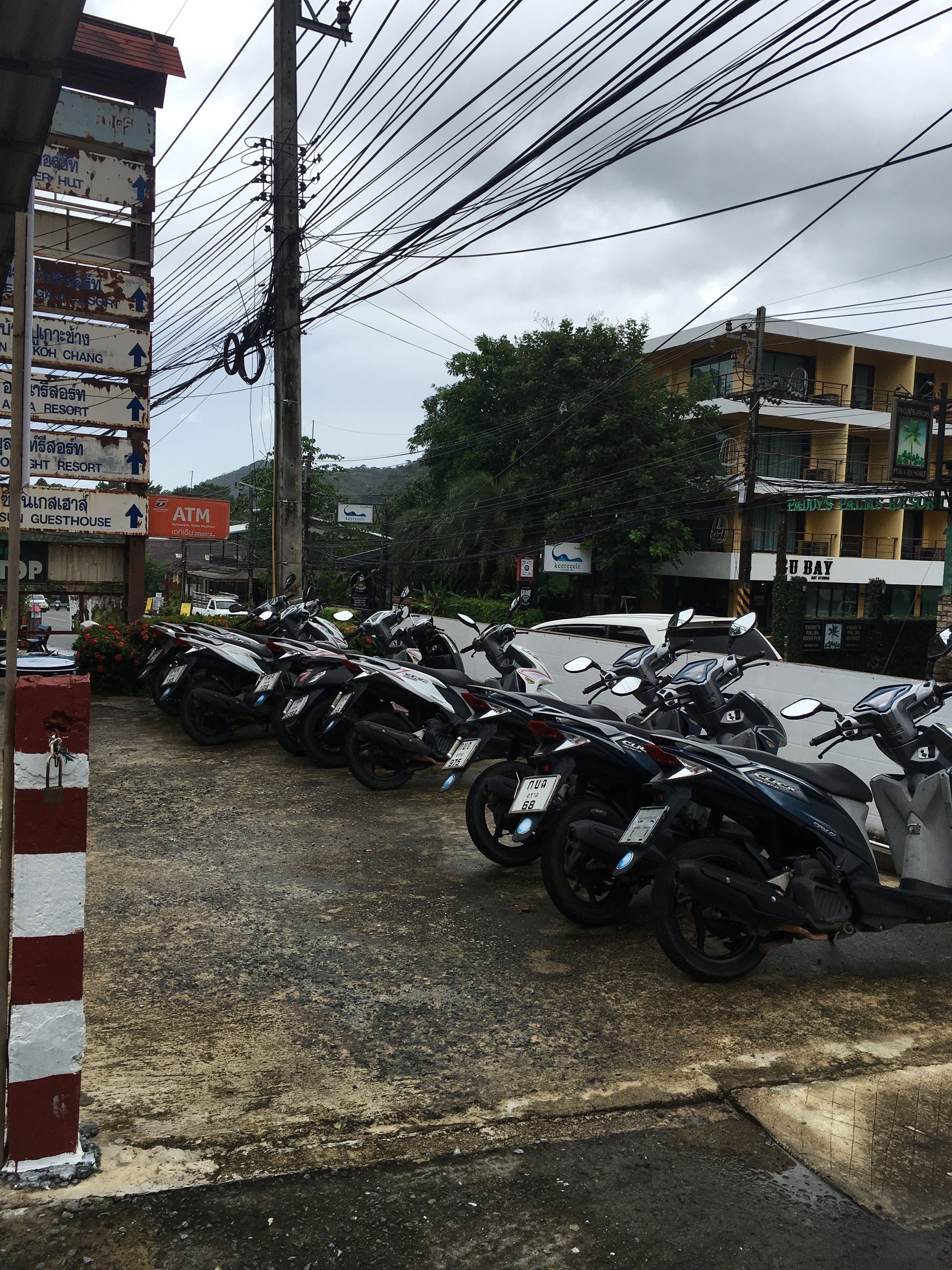 Una fila de motocicletas estacionadas, una señal con indicaciones a varios lugares de interés locales, y un edificio con un cartel que dice 