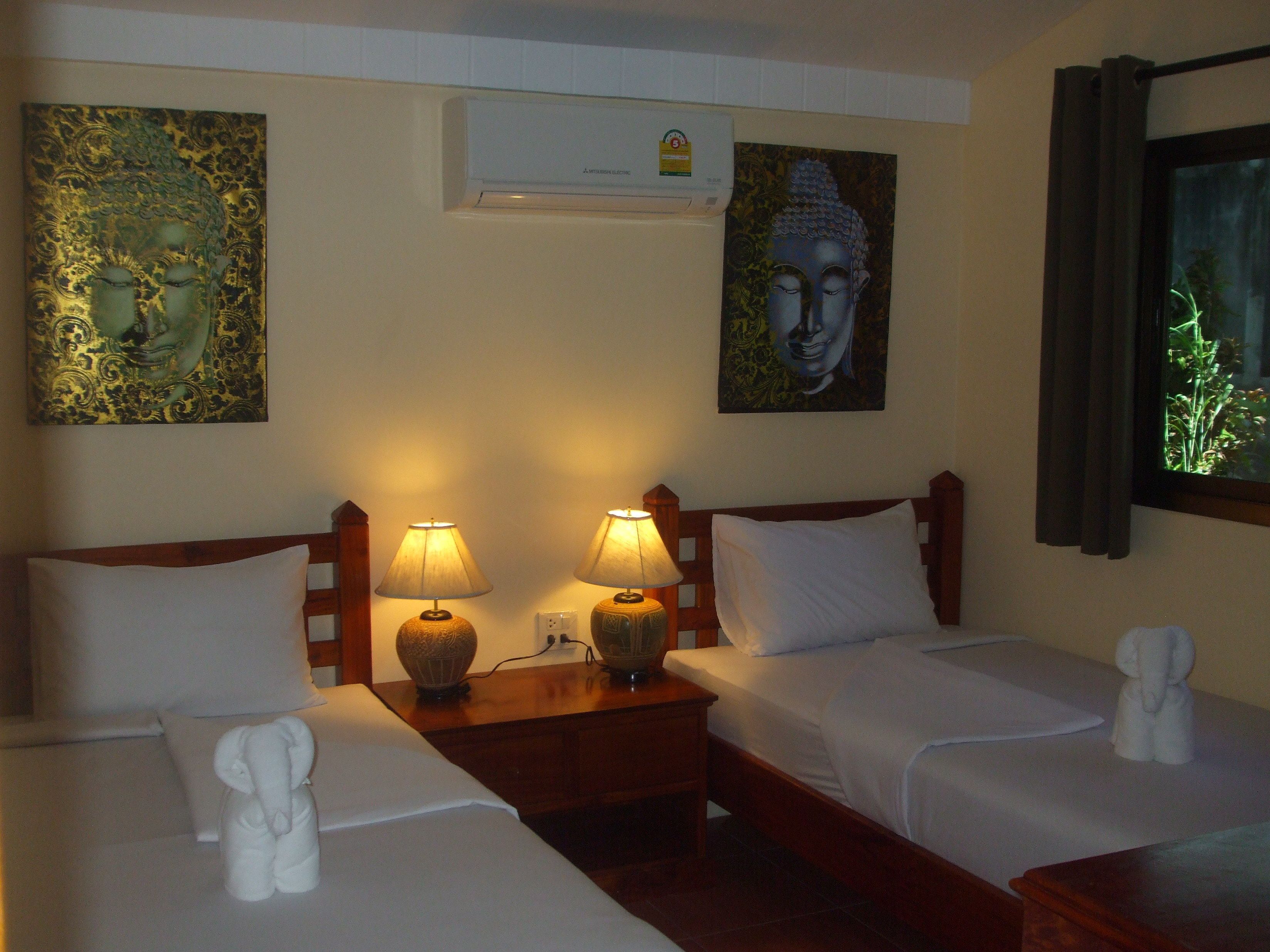 Een hotelkamer met twee bedden, een nachtkastje met lampen en kunstwerken aan de muur.